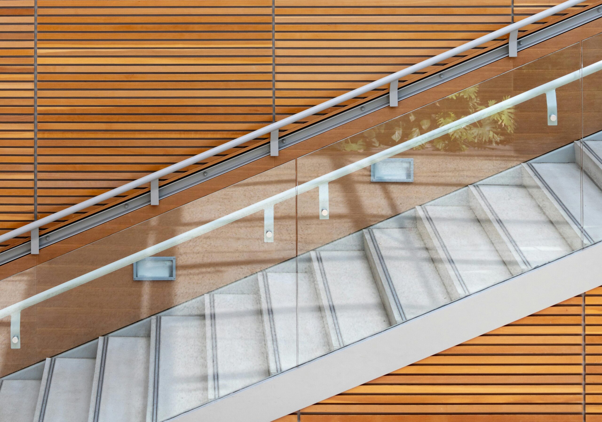 A contemporary staircase featuring glass railings and wooden paneling, highlighting modern architecture.